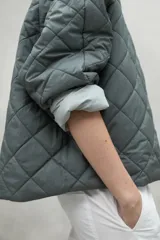 Chaqueta color crema con cuello redondo y cierre frontal con botones a presión.