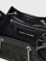 Bolso negro de cuero con textura granulada, con el nombre de la marca grabado en relieve en el frente. Tiene doble asa corta superior y una correa larga de cadena plateada con aplique de cuero en el hombro.