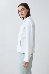 Campera de jean blanca con cuello clásico, bolsillos con solapa abotonados en el pecho y cierre frontal con botones metálicos. Corte recto.