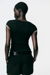 Camiseta negra de corte slim fit, cuello redondo y manga corta. Presenta falsos bolsillos en el delantero y detalle de hilo metalizado en mangas y bolsillos.