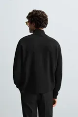 Jersey negro de punto con cuello perkins y cierre frontal de cremallera.