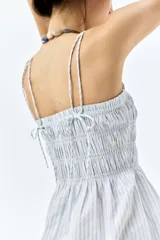 Vestido corto de algodón a rayas celestes y blancas, con cuerpo fruncido, escote cuadrado y breteles spaghetti dobles.