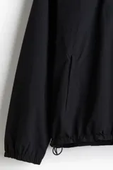Campera rompevientos negra de nylon repelente al agua con protección UV, corte regular, cierre frontal, capucha con cordón de ajuste elástico, puños elásticos, bolsillos laterales y bolsillo interior con cierre, forro de malla y cordón de ajuste elástico oculto en el bajo.
