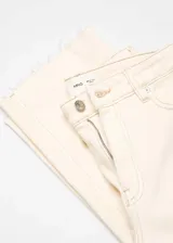 Pantalón de jean color crema, de corte flare y tiro alto, con cinco bolsillos y ruedo desflecado.