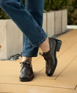 Zapato acordonado de cuero vacuno color marrón oscuro, con suela de goma, horma cuadrada y tacón bajo.