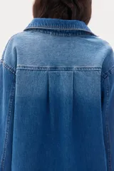Camisa de denim azul con cuello abierto y canesú con pliegue de caja en la espalda. Modelo de corte holgado con hombros caídos y mangas largas con botones a presión en los puños. Bajo recto, algo más largo atrás, con aberturas laterales.