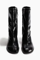 Botines negros de caña media, confeccionados en material con acabado charol brillante. Presentan punta cuadrada, caña ajustada tipo calcetín y un taco ancho y cuadrado.