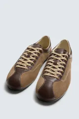 Zapato deportivo de piel color marrón claro con detalles en marrón oscuro y rojo. Presenta pespuntes en contraste, suela plana y cierre con cordones de colores. Colaboración especial Harry Lambert for Zara x Disney.