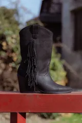 Bota texana negra de cuero con flecos en el lateral exterior, punta marcada, corte clásico, taco de 6cm y caña media de 27cm.