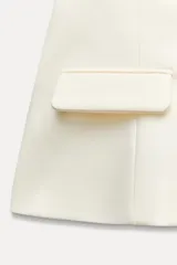 Top negro palabra de honor con escote recto y detalle de pieza metálica en forma de V forrada. Tiene falsos bolsillos con solapa en el delantero, forro interior combinado y cierre lateral con cremallera oculta.