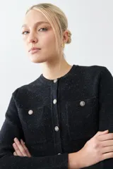 Chaqueta tejida negra con cuello redondo, cierre frontal con botones dorados, bolsillos delanteros y corte clásico.