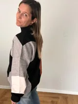 Suéter tejido con diseño geométrico en bloques de color negro, gris, blanco y terracota. Tiene cuello alto tipo polera y corte relajado.