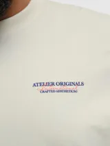 Remera color crema de manga corta con cuello redondo y calce holgado. Estampa en goma ubicada en la espalda con el texto "Atelier Originals Crafted Aesthetics".