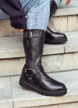 Bota de caña alta color negro, realizada en cuero encerado, con hebillas en la caña y herrajes de níquel. El fondo está realizado artesanalmente, es de suela, y es negro. El interior está forrado en forrería vacuna.