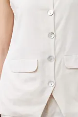 Chaleco color beige con botones de nácar, sin mangas y con bolsillos frontales.