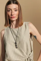 Top sin mangas color beige con finas rayas verticales negras. Presenta un diseño con lazada ajustable en el lateral de la cintura.