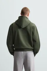 Sudadera negra con capucha ajustable, corte relaxed fit, confeccionada en tejido de algodón compacto con interior en rizo. Cuenta con manga larga, bolsillos frontales tipo canguro, acabados en rib y cierre frontal con cremallera.