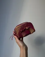 Neceser gris de tela satinada con cierre superior y detalle de moño en el frente.