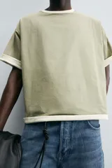 Camiseta color verde claro, de corte holgado, confeccionada en tejido de algodón con interior reversible de popelín. Tiene cuello redondo, manga corta y acabados con vivo combinado a contraste.