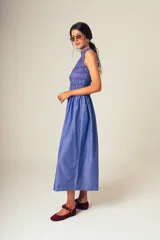 Vestido midi a rayas verticales azules y blancas, con cuerpo superior fruncido y falda amplia. Presenta un detalle de flor roja en el hombro.