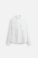 Sobrecamisa blanca de lino, corte relaxed fit, con cuello solapa, manga larga con puño abotonado, dos bolsillos de parche con solapa en el pecho, bajo con aberturas laterales y cierre frontal con botones.