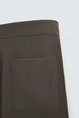 Pantalón marrón de corte ancho, con cintura ajustable con cordón, bolsillos delanteros y traseros tipo parche, detalle de costuras verticales en el frente y cierre frontal con cremallera y gancho metálico oculto.