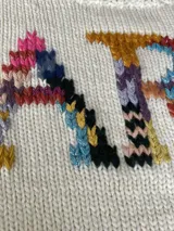 Sweater tejido de lana marrón con cuello redondo y puños acanalados. Presenta un estampado con la palabra 'FARRA' en letras de colores.