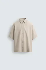 Camisa beige de corte relaxed fit, confeccionada en tejido con algodón, cuello solapa y manga corta.