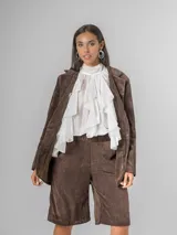 Camisa blanca de algodón italiano con cuello alto ajustable mediante lazo trasero, mangas abullonadas y un gran shabot frontal con volados en cascada.