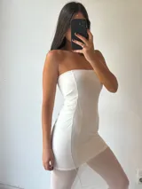 Vestido largo blanco, estilo tubo, sin tirantes (strapless). La parte superior es opaca y ajustada, mientras que la falda es de tela transparente que deja ver las piernas.