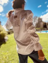 Camisa marrón de algodón con cuello clásico, cierre frontal con botones dorados y mangas largas abullonadas con puños elásticos.