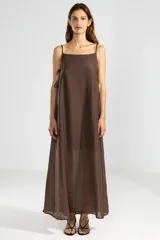 Vestido largo color marrón chocolate, de breteles finos y escote recto. Presenta lazos ajustables en los laterales, forro hasta arriba de las rodillas y ruedo asimétrico.