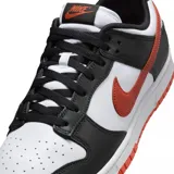 Zapatilla de corte bajo Nike Dunk Low Retro, con base blanca y superposiciones de cuero negro. Presenta el logo Swoosh y detalles en color naranja quemado (burnt orange) en el lateral, talón y suela exterior.