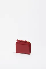 Monedero pequeño de estructura rígida, color negro, con cierre de cremallera y tirador de tejido amarillo mostaza. Presenta un bolsillo exterior frontal y el logo de la marca grabado en dorado.