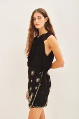 Minifalda negra con short interno, de corte cruzado con lazo lateral y bordados florales en frente y espalda.
