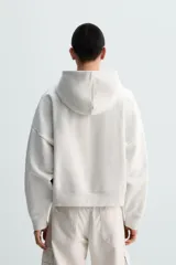 Sudadera con capucha color crudo, corte boxy, manga larga y bolsillo tipo canguro.
