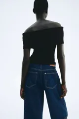 Top negro con textura, corte ajustado y escote off-the-shoulder con volantes.