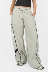 Pantalón deportivo gris de nylon, de calce recto y tiro medio, con elástico en la cintura, cordones ajustables y detalle de recorte con vivo a contratono en los laterales.