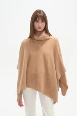 Poncho tejido color tostado, con cuello alto tipo tortuga y diseño asimétrico en el ruedo.
