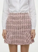 Pollera corta de tiro alto confeccionada en tejido tweed con estampado a cuadros en tonos rosados y negros. Presenta un ruedo con volado.