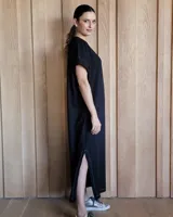 Vestido largo color crudo con cuello redondo y mangas cortas con ribete negro. Tiene corte recto y aberturas laterales en el ruedo.
