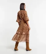 Vestido largo de chiffon con estampa de corazones con diseño de leopardo. Tiene cuello alto con lazo, mangas largas ligeramente transparentes y falda con volado. El tejido contiene hilo metalizado.