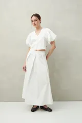 Falda midi blanca con pequeños lunares negros, de corte acampanado y cintura alta con pliegues.