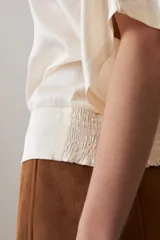 Blusa color beige, de tela satinada, con mangas cortas y cuello redondo.