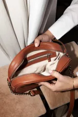 Cartera bandolera negra con diseño capitoneado en forma de V, correa de cuero y cadena plateada, cierre metálico y doble bolsillo interior.