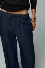 Pantalón de jean azul oscuro, de tiro alto y pierna ancha, con cintura elástica ajustable con cordones y bolsillos delanteros.
