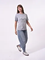 Remera blanca de algodón con cuello redondo y manga corta. Presenta un pequeño bordado en el pecho izquierdo con una figura que parece ser una persona acostada en una tabla de surf o flotador.