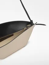 Bolso de hombro de cuero color beige y negro, con forma geométrica asimétrica y asa fina negra.