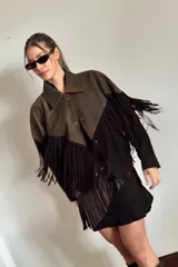 Chaqueta bomber de cuero ovino marrón desgastado y gamuza color chocolate, con cuello clásico, cierre frontal con botones a presión y mangas largas con puños ajustados. Presenta flecos largos en la parte inferior y en las mangas.