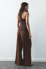 Pantalón color ladrillo de tiro medio con trabillas, detalle de pliegues, bolsillos laterales y falsos bolsillos de vivo en la espalda. Cierre frontal con cremallera y botón.
